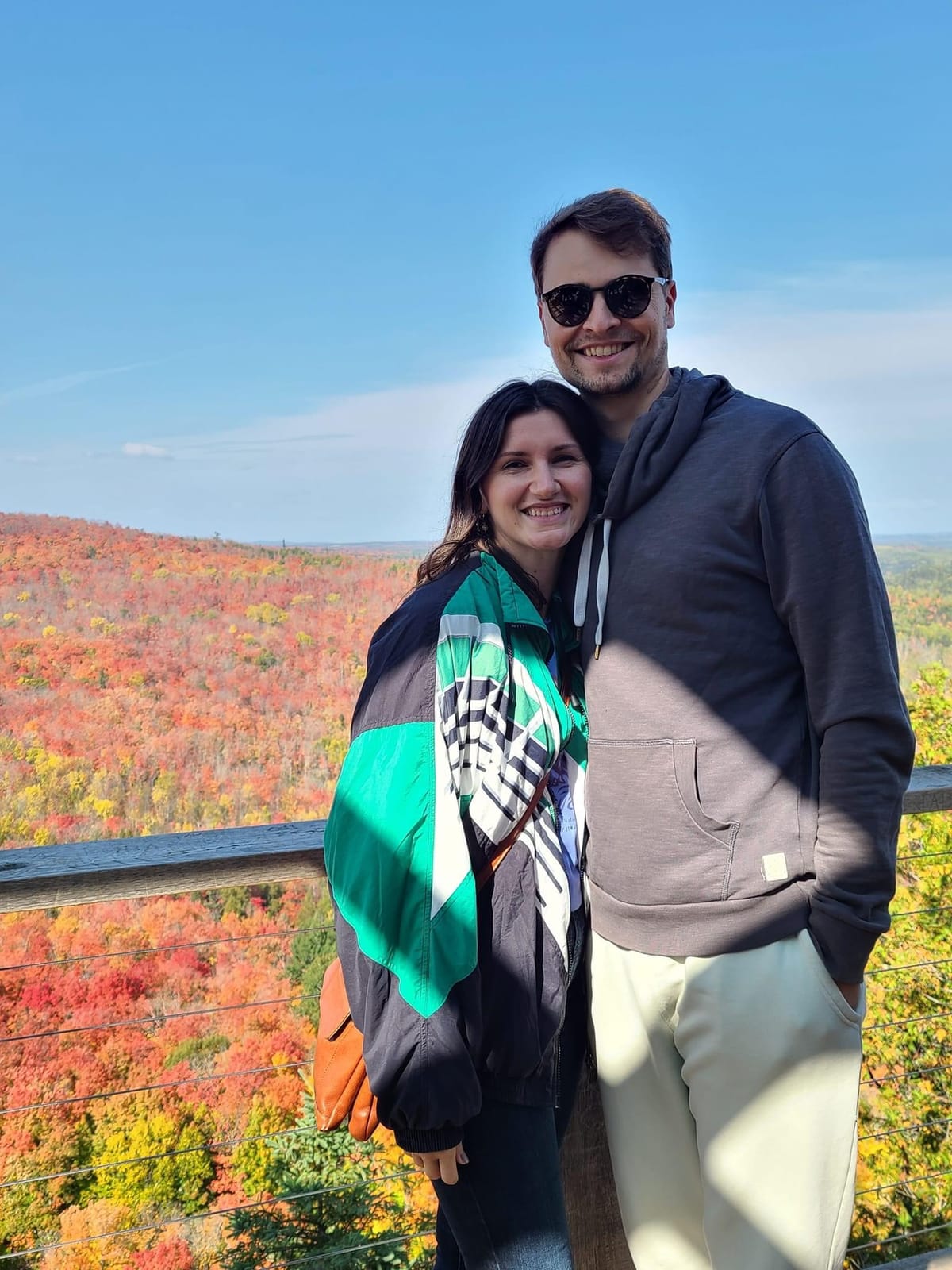 Connor and his partner Jillian pose arm-in-arm in front of the fall-colored forest